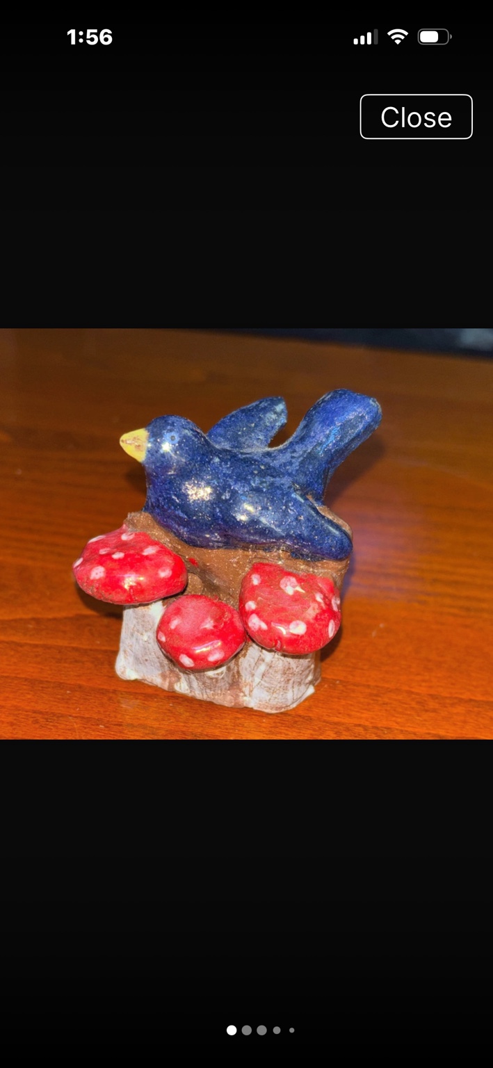 Small blue bird figurine perched over red mushrooms